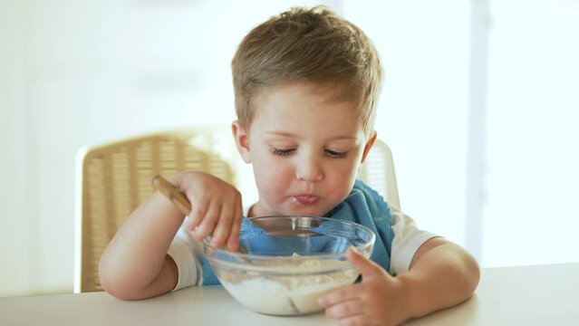 Baby eats cereal porridge. Bboy is holding spoon in his hand. Child sits at table and eats porridge.Family breakfast in kitchen. Feeding child at table.Child proper nutrition.Breakfast in kindergarten