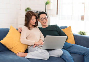 Asian couple watching movie in computer laptop together on sofa in living room at home. family lifestyle concept.