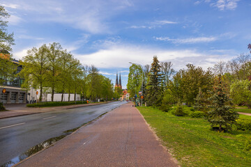 Fototapeta na wymiar Cityscape view of road with green trees on sides and famous church towers on background. Sweden. 