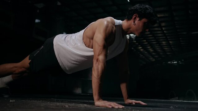 4K Strong Asian sportsman do sport training workout push ups exercise on the floor in abandoned building. Active man bodybuilder athlete practicing muscular build body weight training in dark old gym