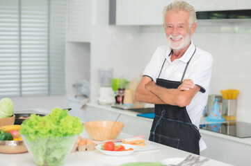 Happy smiling senior Caucasian man standing arms crossed in kitchen at home