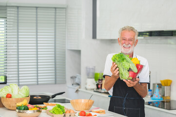 Happy smiling senior Caucasian man holding vegetables bowl in kitchen at home