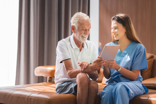 Asian nurse or caregiver teaching senior Caucasian man to handle with digital tablet computer at home