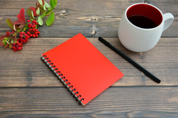 red notepad with black pen and cup of tea on wooden background