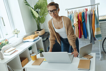 Cheerful young woman looking at camera while standing in fashion store office