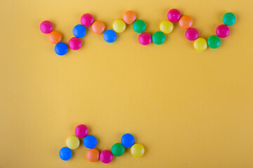Top view on different color chocolate round buttons lay on zigzag shape on yellow background. Frame, copy space for text