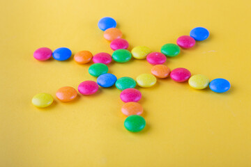 Front view on variety of round button shaped chocolate sweets lay like sun with rays on yellow background
