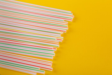 Heap of striped drinking straws, tubules lay on yellow background. Copy space for text. Top view, flat lay