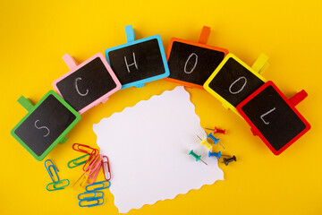 Back to school stationary. Blank paper, copy space for text, paperclips, pins. Word school written on small blackboards lay on yellow background. Top view, flat lay