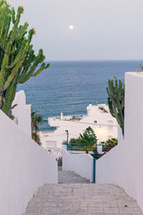 Full moon over the sea, viewed from a narrow street of a village with white houses on the...