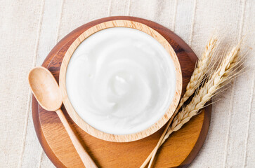 Greek yogurt in a wooden bowl and dry barley on table.