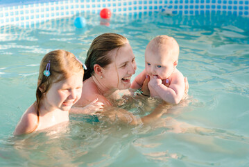 Family playing in the swimming pool. Mother and kids having fun in the pool. Summer leisure and holidays and vacation concept. People swim in a metal frame pool in the backyard.