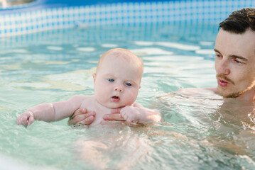 Baby swimming. Hand father, swimming instructor hold happy little boy in a paddling pool. Teaches...