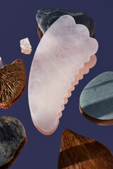 Pink Gua Sha massager on mirror background. Pink jade stone for face and body care. Vertical shoot. Flat lay, top view.