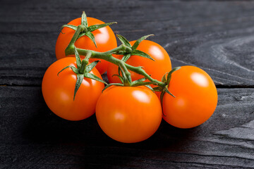 orange cherry tomatoes on a branch on dark wooden table