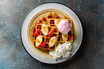 waffles with fresh strawberries, bananas and powdered sugar and ice cream on blue stone table