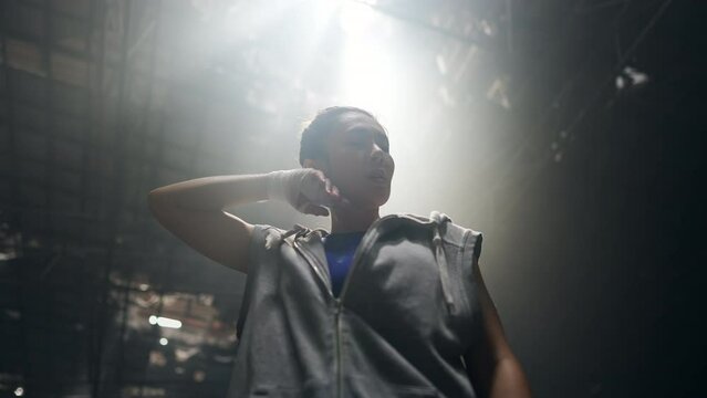 4K Strong Asian sportswoman athlete do combat sport training workout boxing exercise with punching bag in abandoned building. Active woman boxer practicing fighting exercise kickboxing in dark old gym