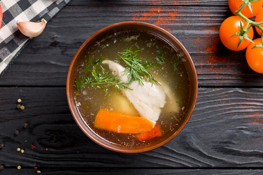 Chicken soup bouillon with vegetables and chicken meat on bowl on dark wooden table