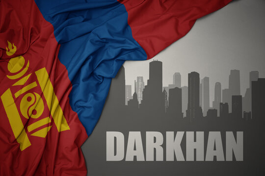 abstract silhouette of the city with text Darkhan near waving national flag of mongolia on a gray background.3D illustration