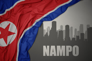 abstract silhouette of the city with text Nampo near waving national flag of north korea on a gray background.3D illustration