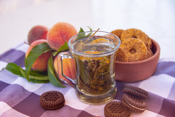 Still life - a transparent cup with herbal tea, cookies and peaches on the background. Beautiful photo of healthy and wholesome food. Medicinal herbal tea with fruits and biscuits.