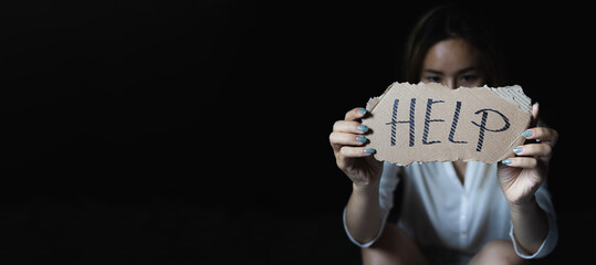 Women sitting alone with depressed expression and showing a paper with a help text. Stop violence...