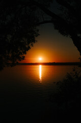 Fototapeta na wymiar Beautiful natural landscape, orange sunset on lake in frame of trees. Sun and reflection on water, vignette