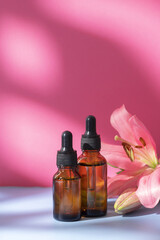 Nature cosmetic in glass bottles with lily flower and shadow on pink background. Face and body care spa concept. Hyaluronic acid oil, serum with collagen and peptides skin care product
