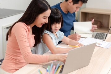 Beautiful Asian women are teaching cute girls to study online and handsome men are working using laptops over the internet on their desks at home. It's a new normal life for the family.