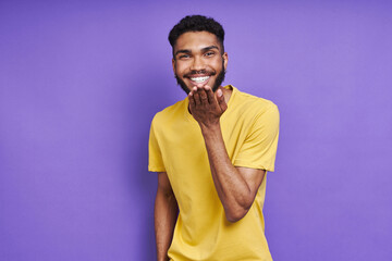Handsome African man blowing a kiss and smiling while standing against purple background