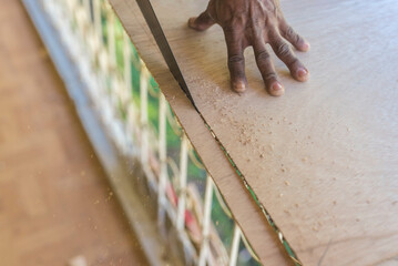 An anonymous carpenter saws off a small piece of plywood with a crosscut handsaw. - obrazy, fototapety, plakaty