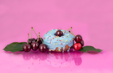 Close-up of a blue donought with red cherries reflected on a pink background. There are also cherry leaves to see. There is room for text