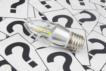 Saving electric energy problems and solutions concept. LED light bulb on many question marks close-up.