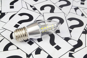 Saving electric energy questions concept. LED light bulb on many question marks.
