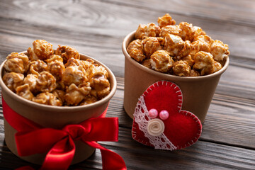 Carton buckets with caramelized popcorn and valentine decorations on kitchen table food background