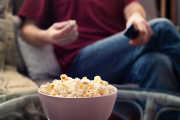 Caucasian man sitting on sofa with popcorn and tv remote