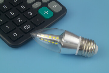 Led light bulb and calculator on blue background. Save money and electric energy using led light concept.