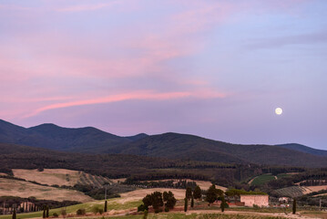 Landschaft in der Toskana mit Hügeln, Häusern und Straße bei Sonnenuntergang mit Mond