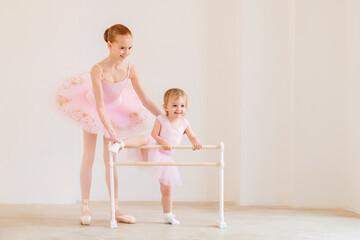 The older sister, a ballerina in a pink tutu and pointe shoes, shows the baby how to practice at...