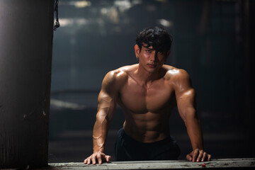 Portrait of Asian sportsman athlete in sportswear do sport training workout exercise bodybuilding in abandoned building. Active man bodybuilder practicing muscular strength training in dark old gym