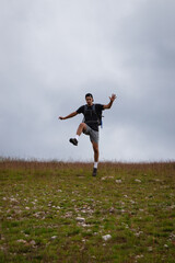 Fototapeta na wymiar Swarthier type of man is running down a gravel hill, checking his every step to avoid injury. Active athlete runs over challenging terrain to improve fitness, coordination and precision of movement