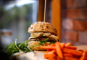 Burger w artystycznej kompozycji z frytkami i batatami oraz cebulą pieczarkami. Burgerownia - zdjęcie świeżego, apetycznego burgera