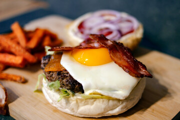 Burger w artystycznej kompozycji z frytkami i batatami oraz cebulą pieczarkami. Burgerownia - zdjęcie świeżego, apetycznego burgera