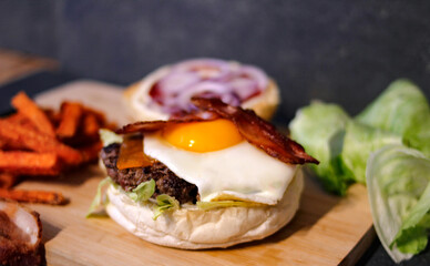 Burger w artystycznej kompozycji z frytkami i batatami oraz cebulą pieczarkami. Burgerownia - zdjęcie świeżego, apetycznego burgera