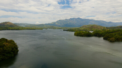 Fototapeta na wymiar Tropical landscape: A lake against the background of mountains and tropical vegetation. Loggal Oya Reservoir. Sri Lanka.