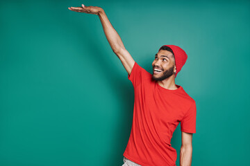 Fototapeta premium Handsome African man showing height and smiling while standing against green background