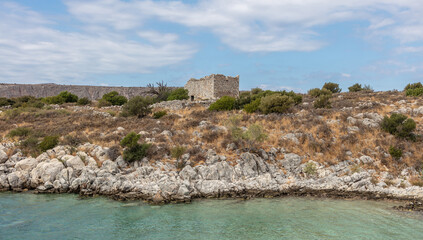 Fototapeta na wymiar Greece. Mani Laconia, Peloponnese. Ruin old stone building on rocky land, calm sea, cloudy blue sky.