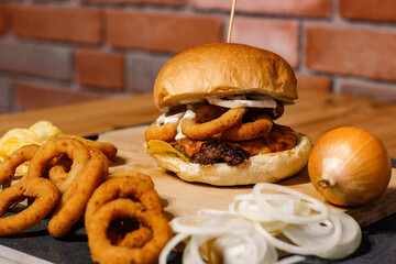 Burger w artystycznej kompozycji z frytkami i batatami oraz cebulą pieczarkami. Burgerownia - zdjęcie świeżego, apetycznego burgera