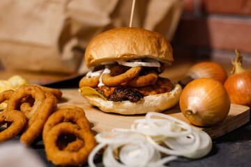 Burger w artystycznej kompozycji z frytkami i batatami oraz cebulą pieczarkami. Burgerownia - zdjęcie świeżego, apetycznego burgera