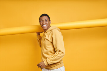 Happy African man carrying rolled up yellow wallpaper while standing against yellow background